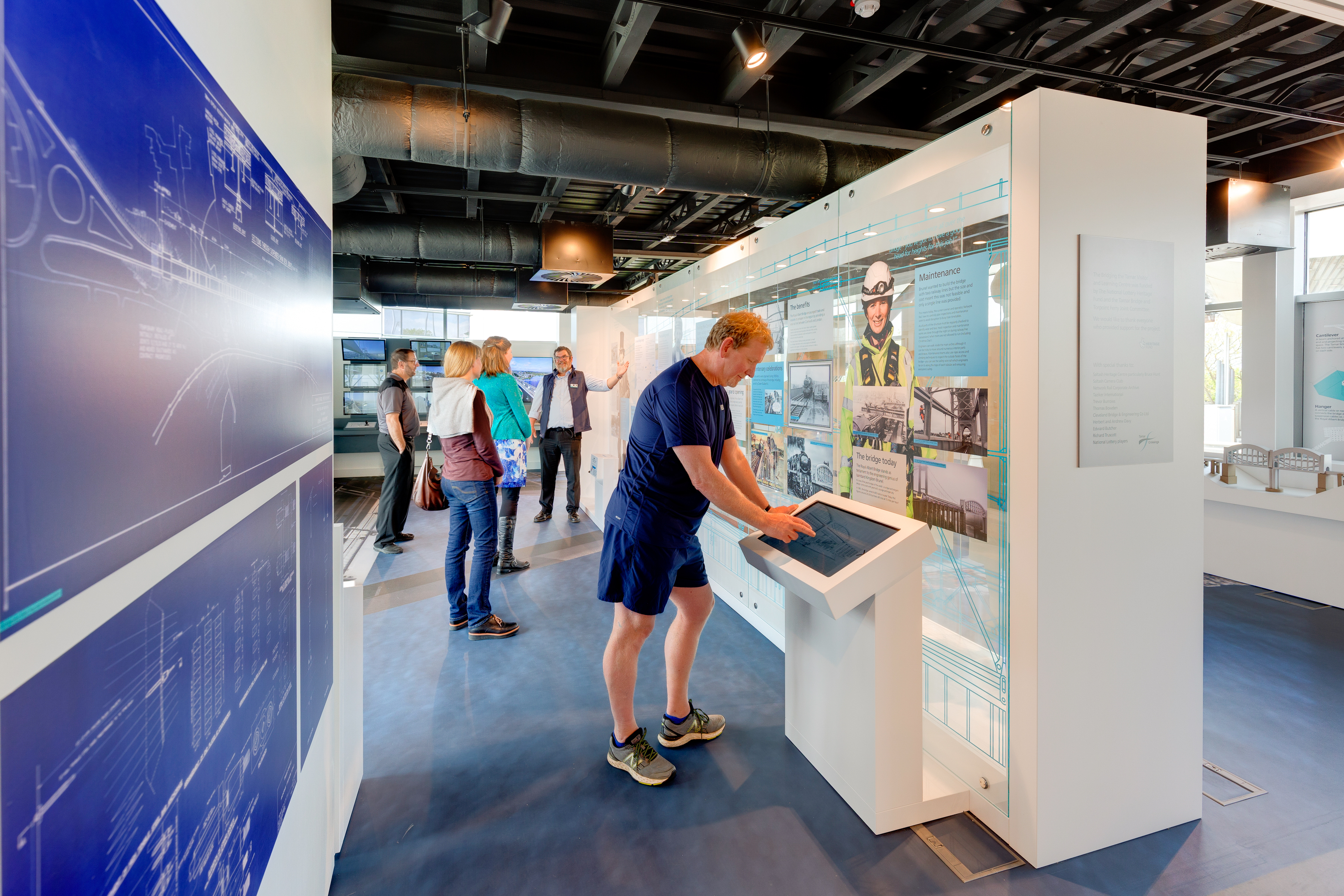 Guide showing visitors round, whilst someone else looks at a touchscreen in the Bridging the Tamar Visitor Centre